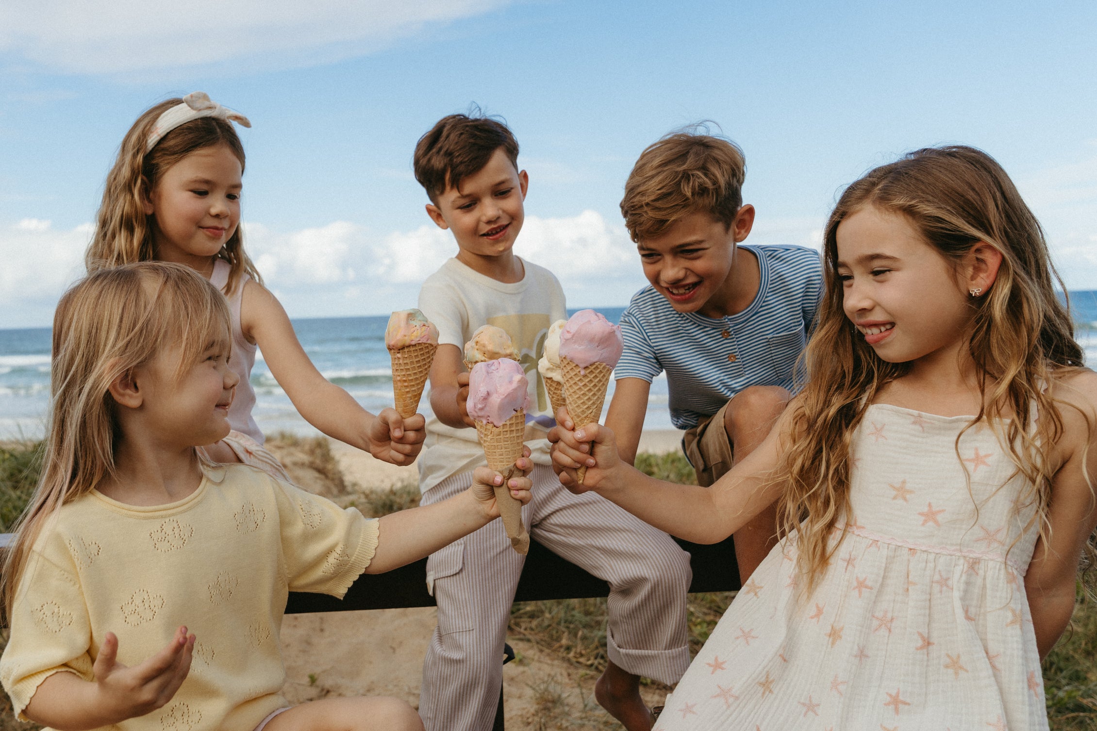Children with ice cream cones sitting on a bench by the ocean. Yes mila brand.